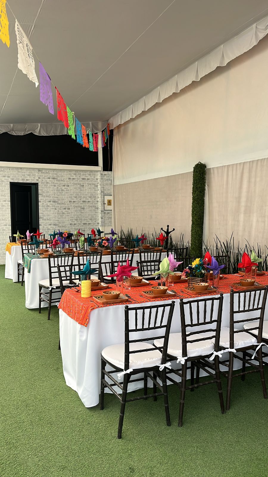 Carpa con papel picado y mesas largas con caminos naranjas y vajilla de barro