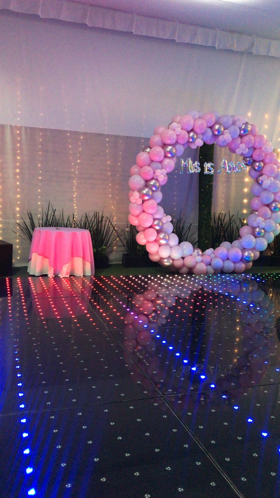 Aro de globos rosados con leyenda de XV años sobre la pista de baile LED