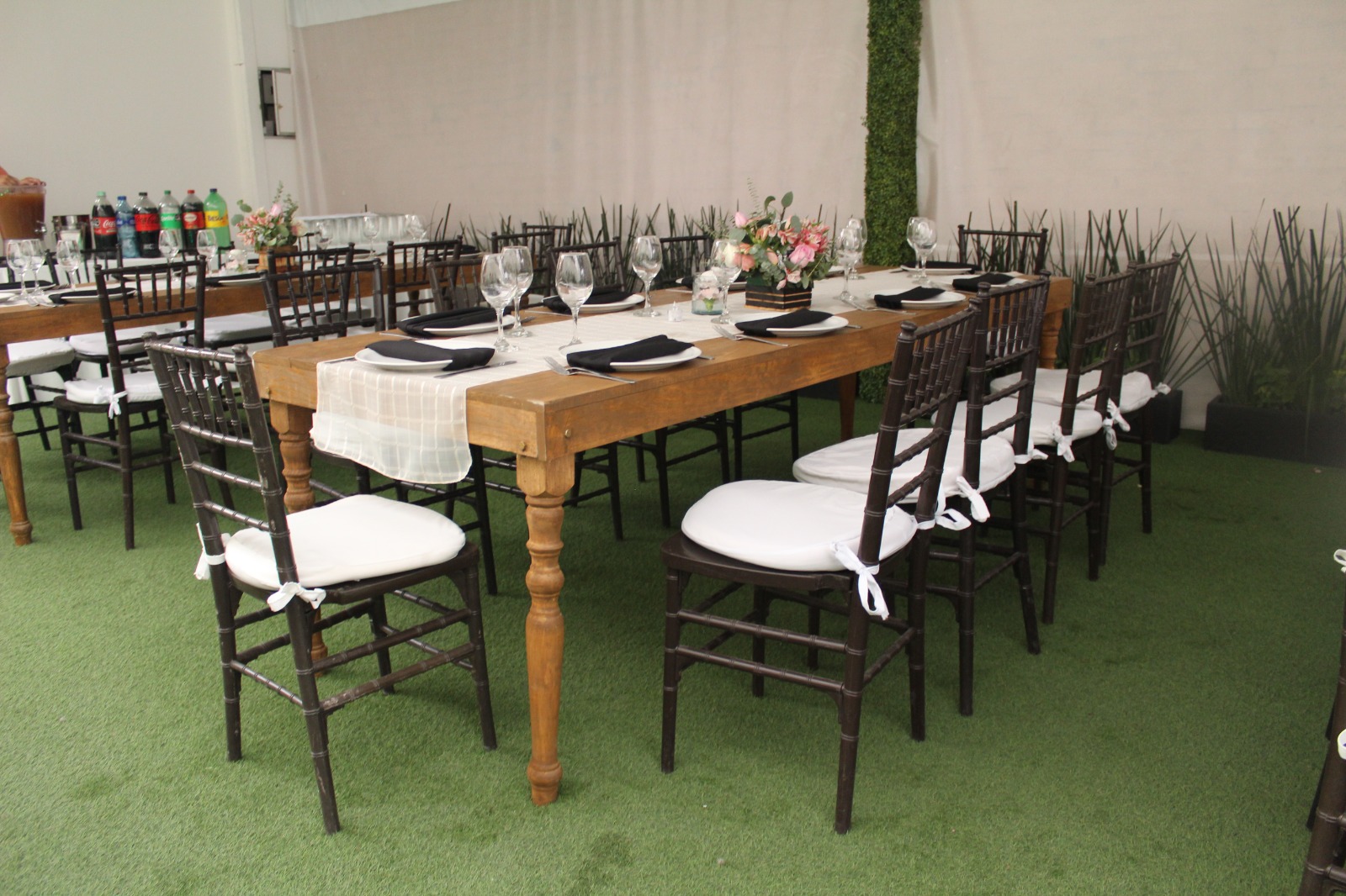 Mesa de madera vintage con sillas negras de cojín blanco, servilletas negras y flores rosas