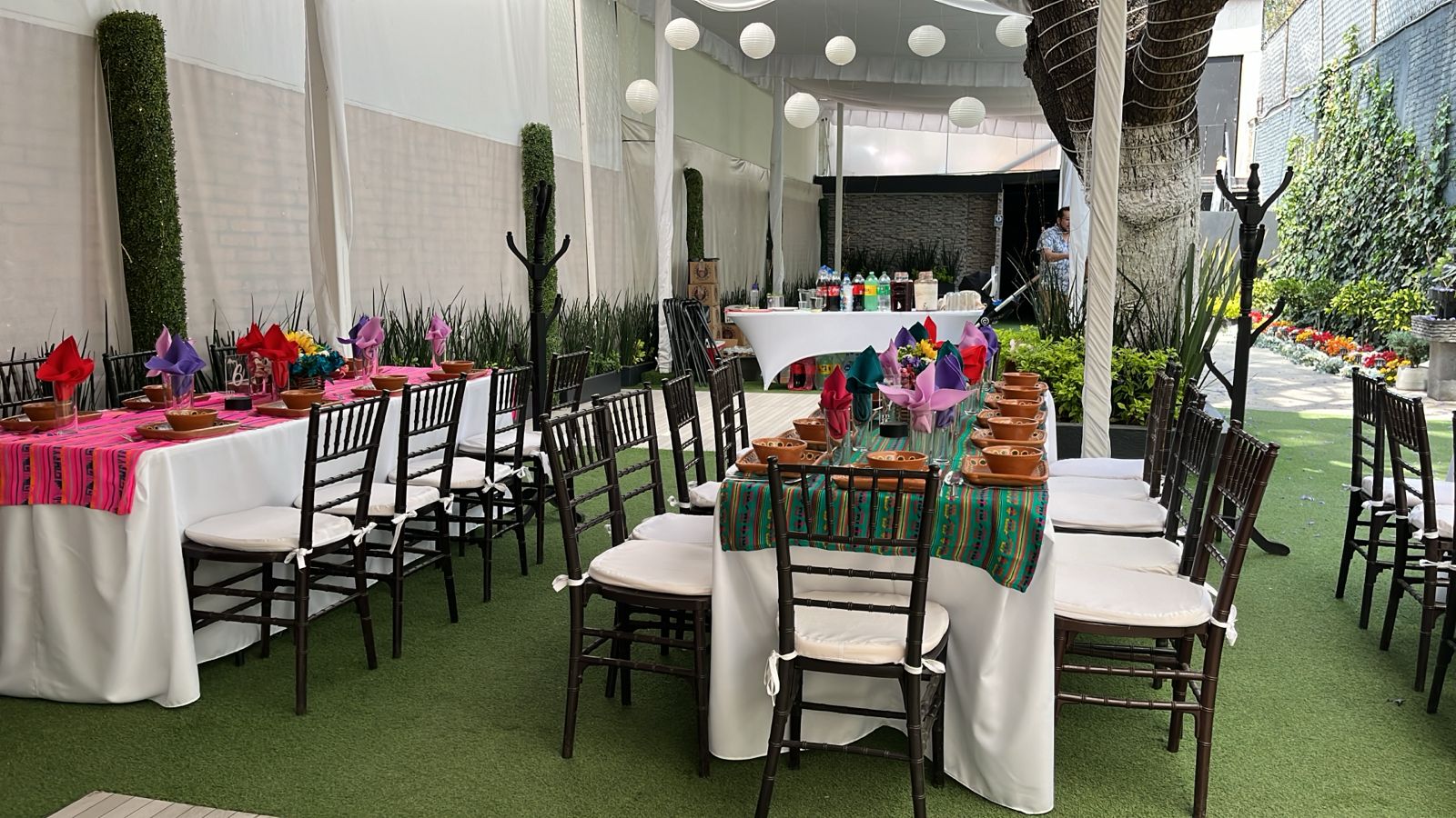 Jardín con mesas vestidas de blanco, caminos rosa y verde mexicano y vajilla de barro