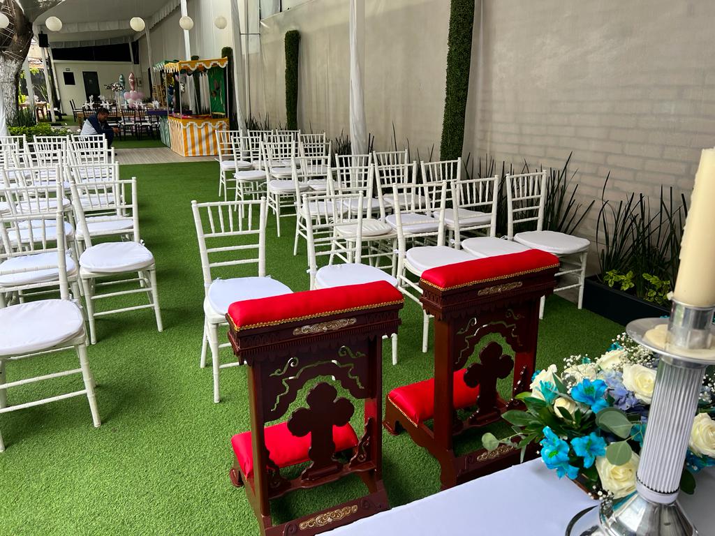 Reclinatorios de madera con cojines rojos frente al altar con flores azules y blancas