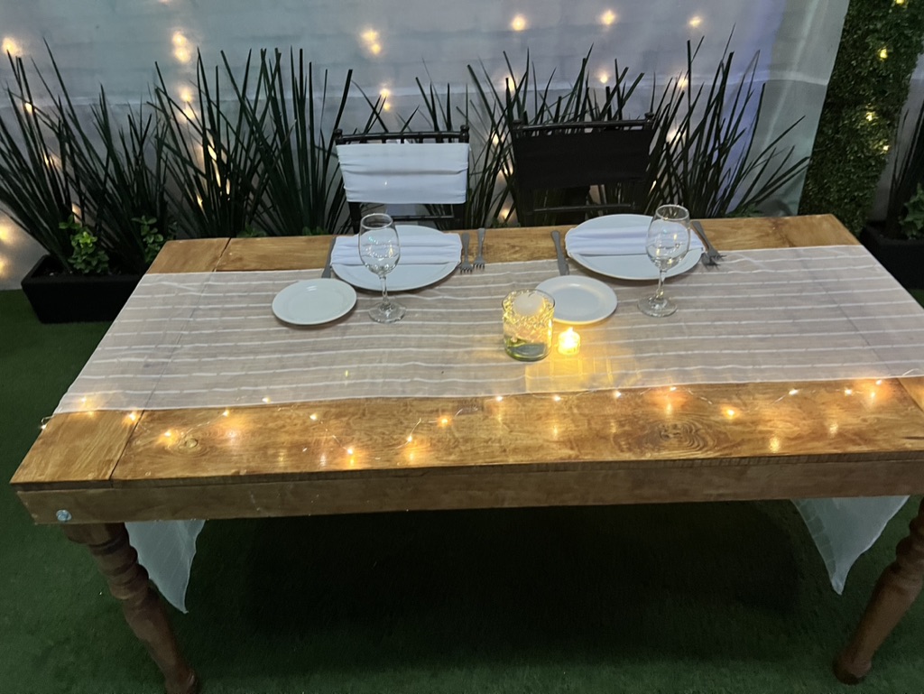 Mesa rústica para dos lugares con mantel de gasa y velas bajo las luces