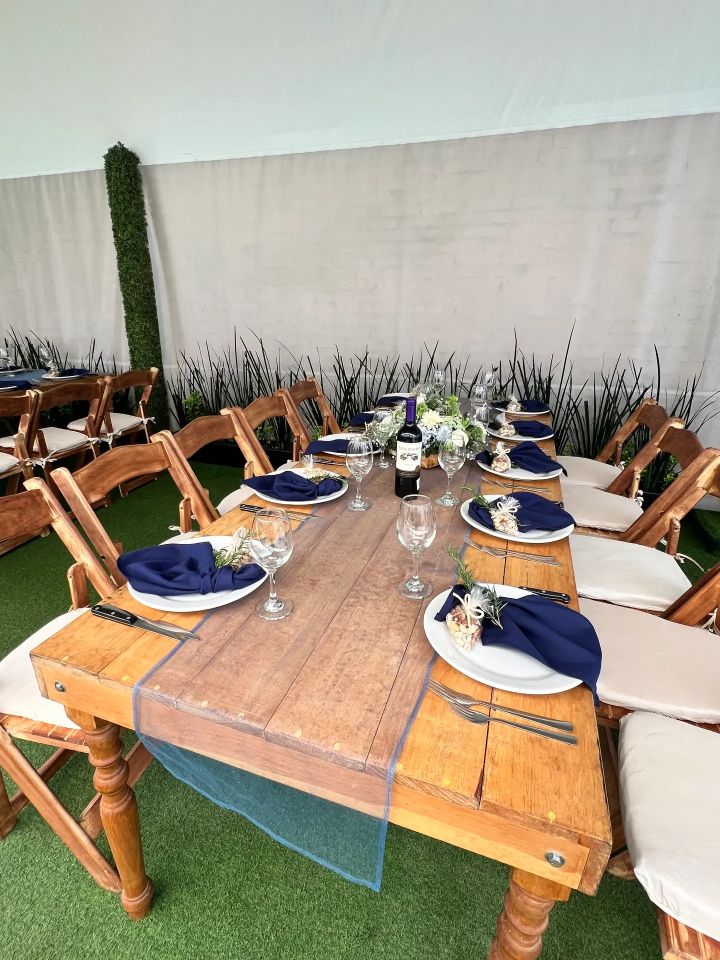 Mesa larga de madera con servilletas azul marino, romero y detalles de bienvenida