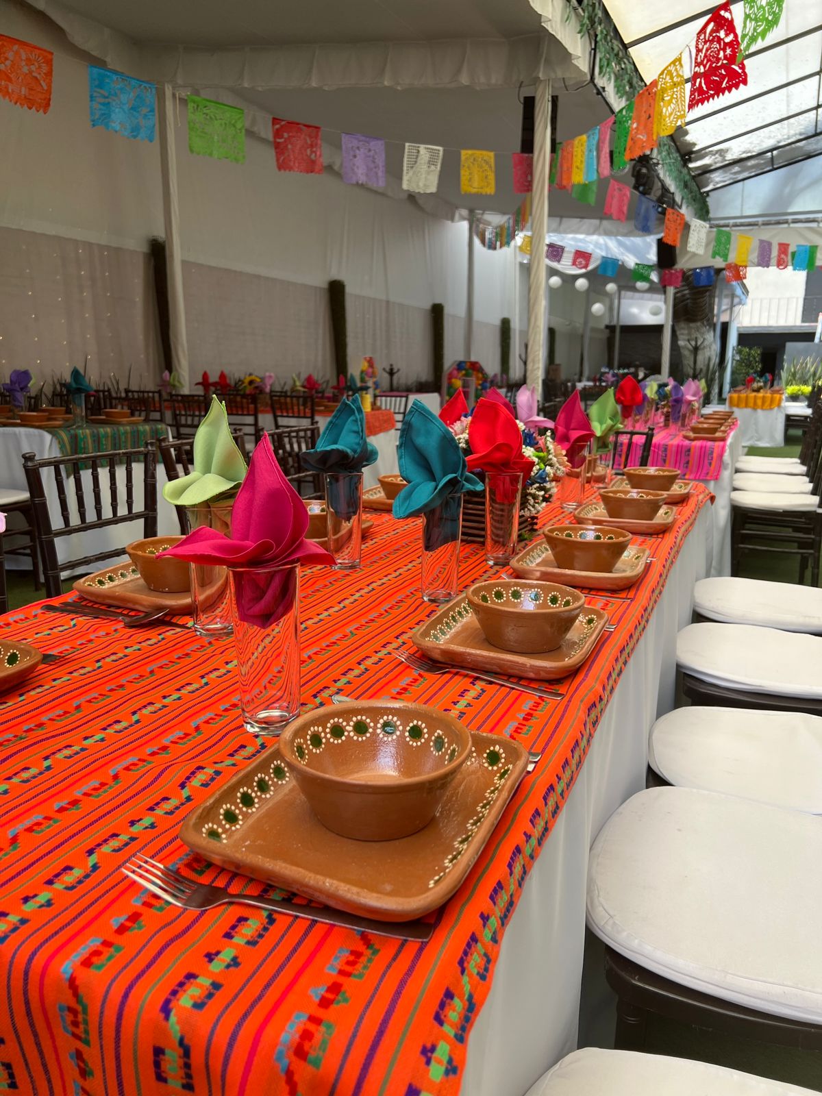 Mesa larga con mantel naranja mexicano, vajilla de barro y servilletas de colores