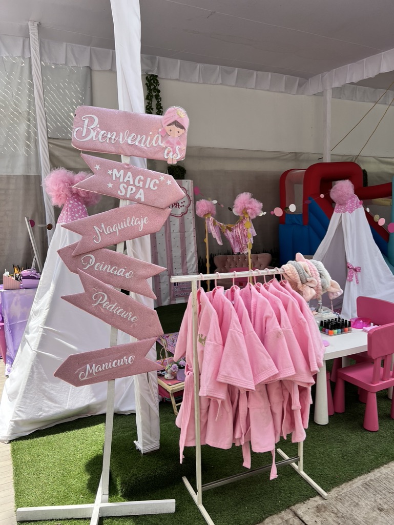 Letrero de bienvenida con batas rosas y estaciones de spa para niñas