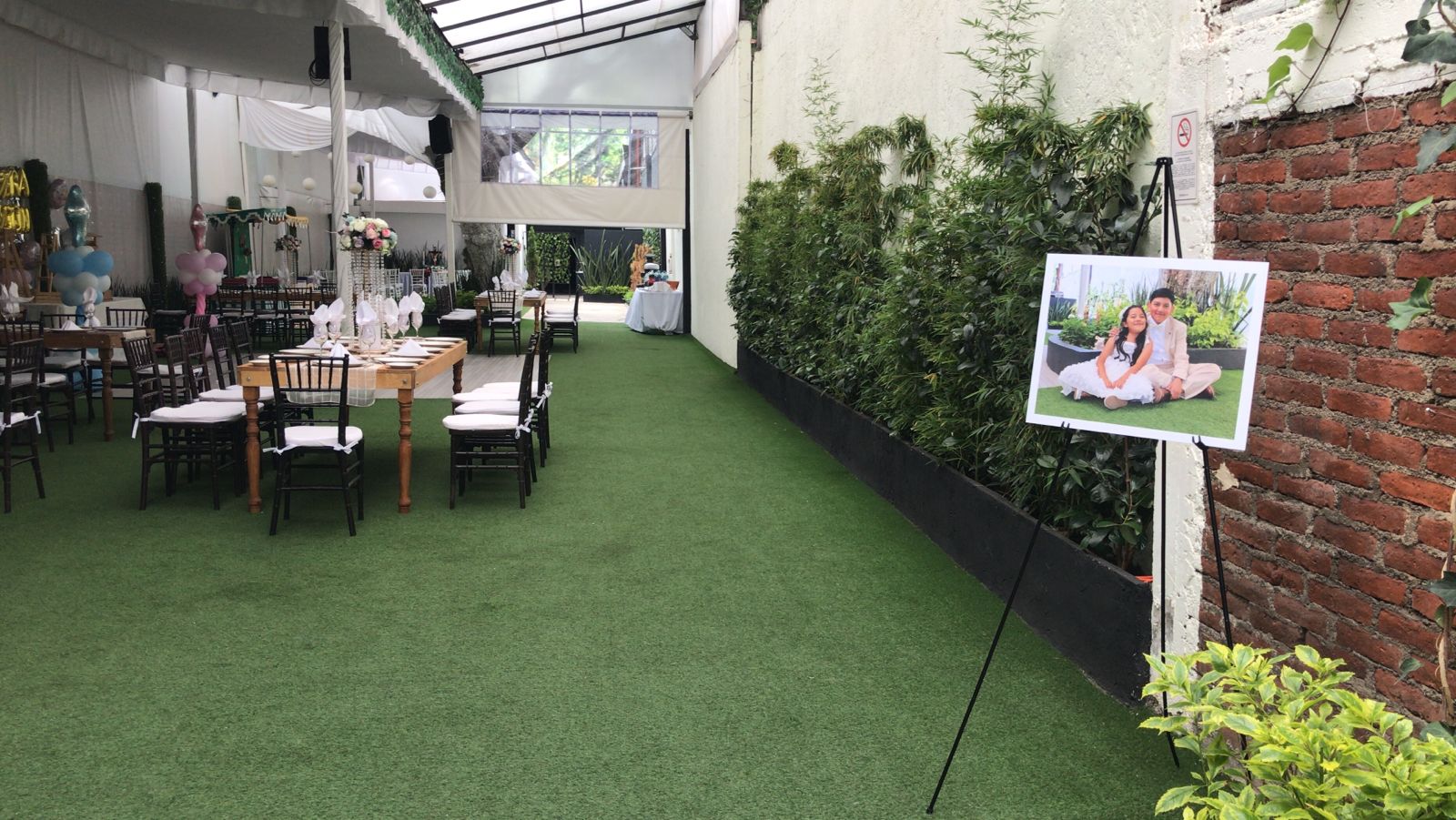 Pasillo verde con caballete de bienvenida para quinceañera junto a las mesas
