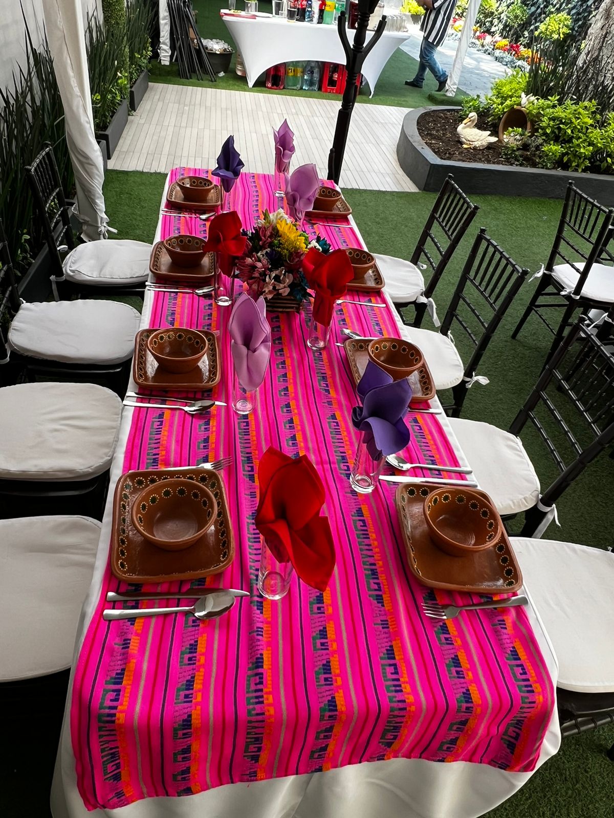 Mesa con camino rosa mexicano, vajilla de barro, flores y servilletas moradas y rojas