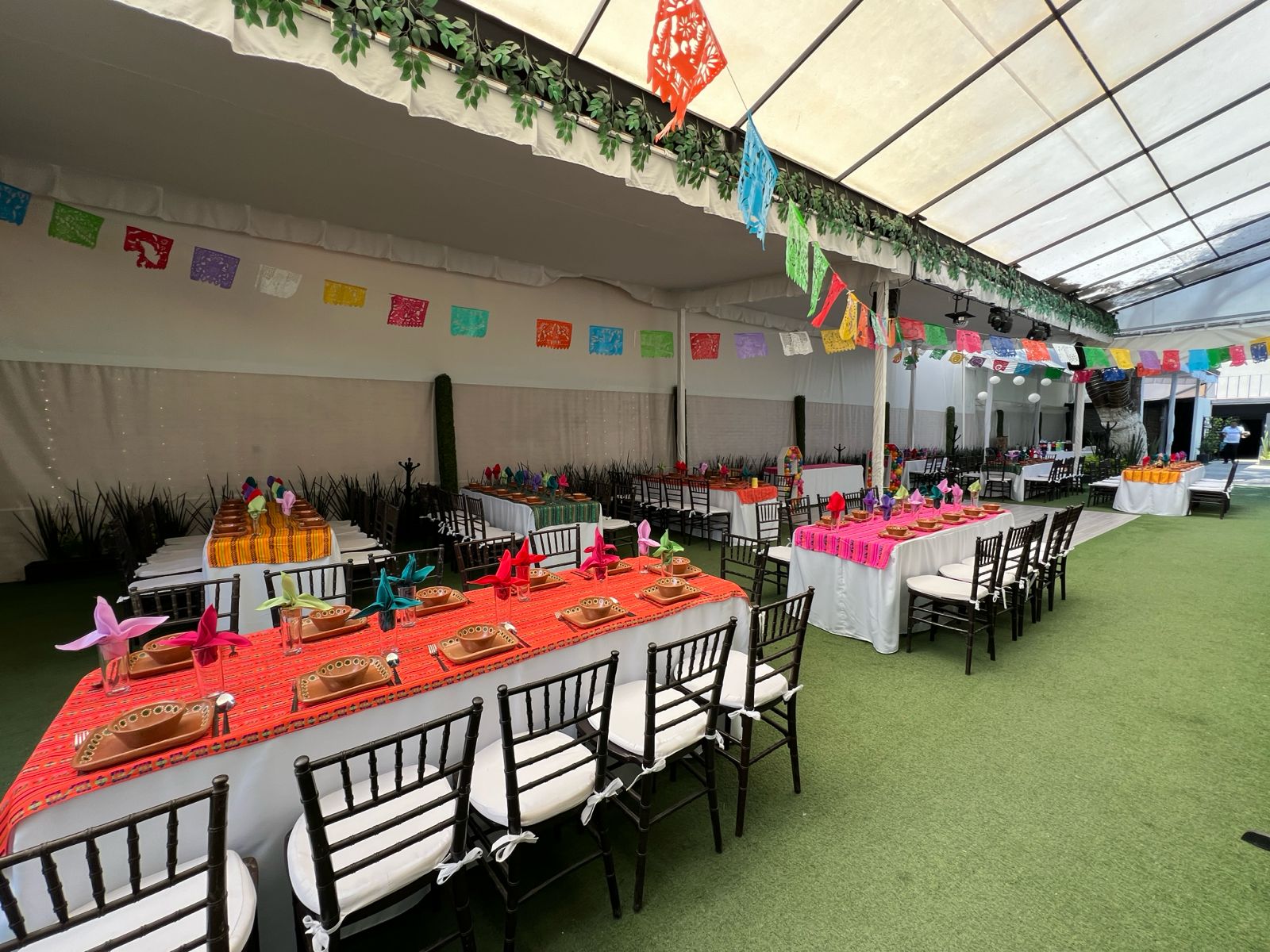 Carpa del jardín con papel picado de colores y mesas largas con caminos mexicanos