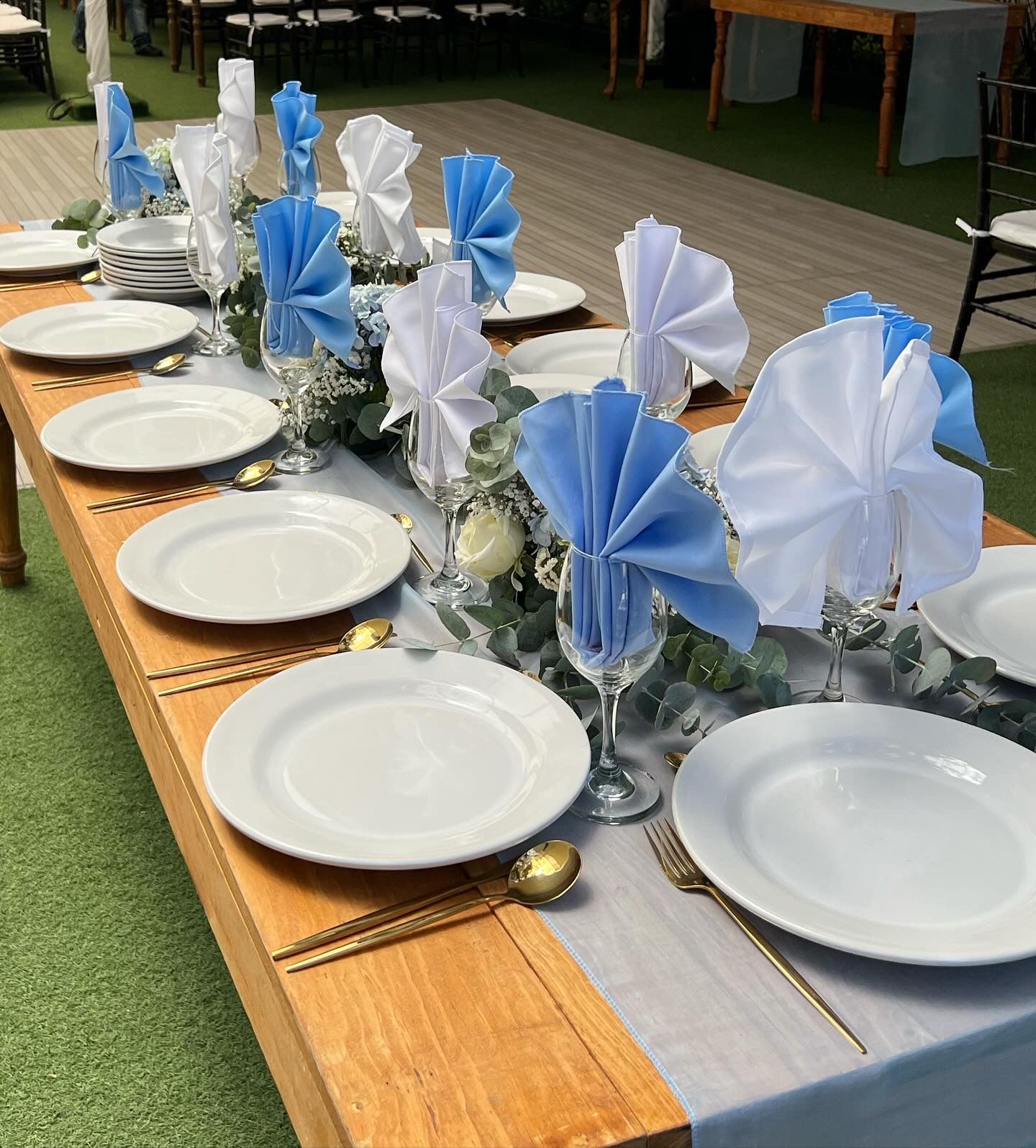 Mesa larga con servilletas azules y blancas en copas y cubiertos dorados