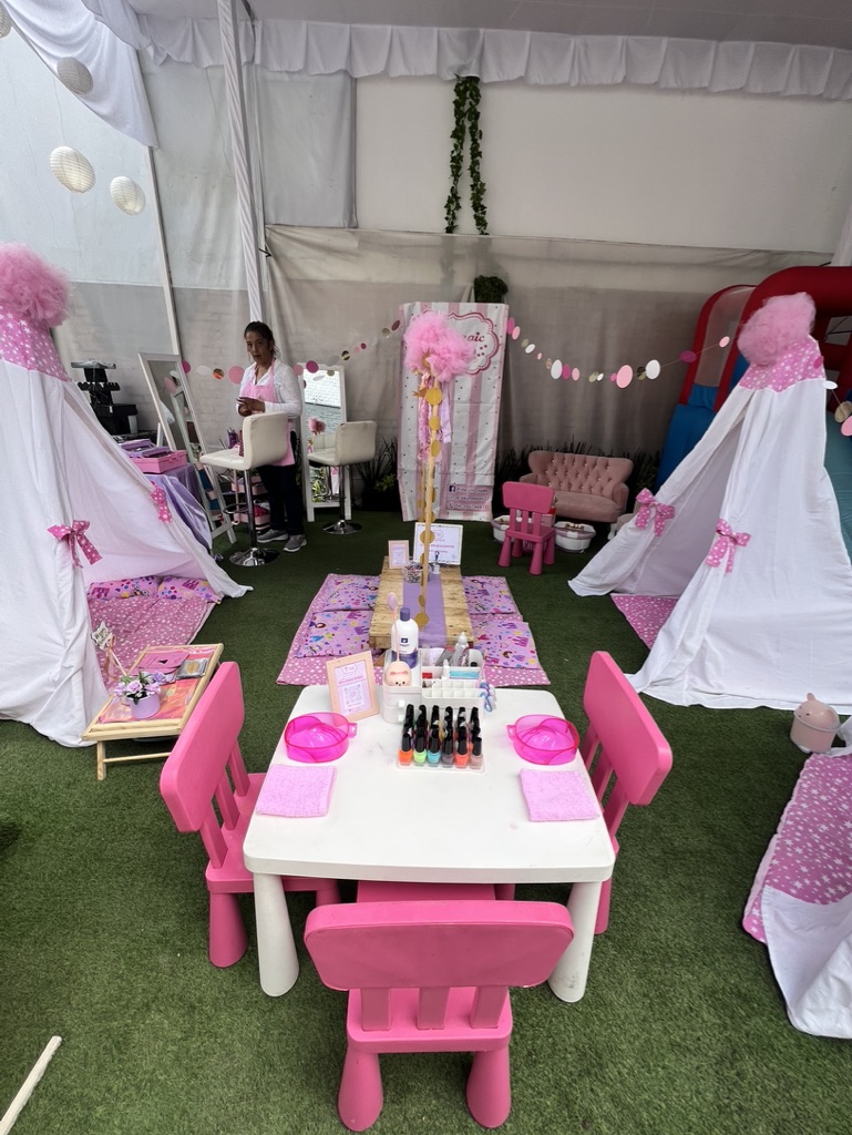 Zona spa infantil con carpas tipi blancas, mesa de manicure y decoración rosa