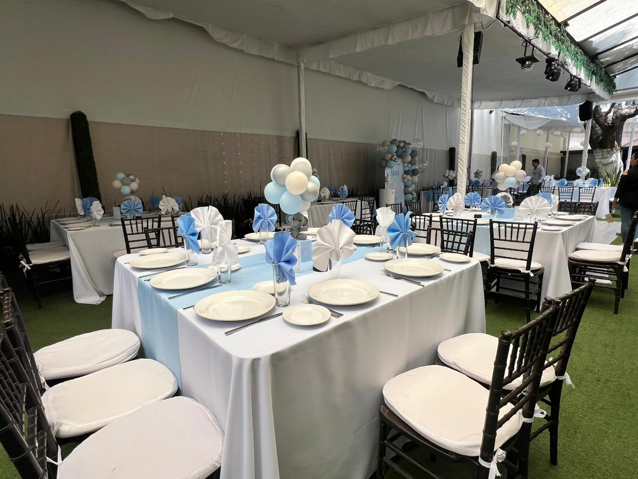 Mesas con mantel blanco y camino azul claro, globos azul y blanco y sillas negras