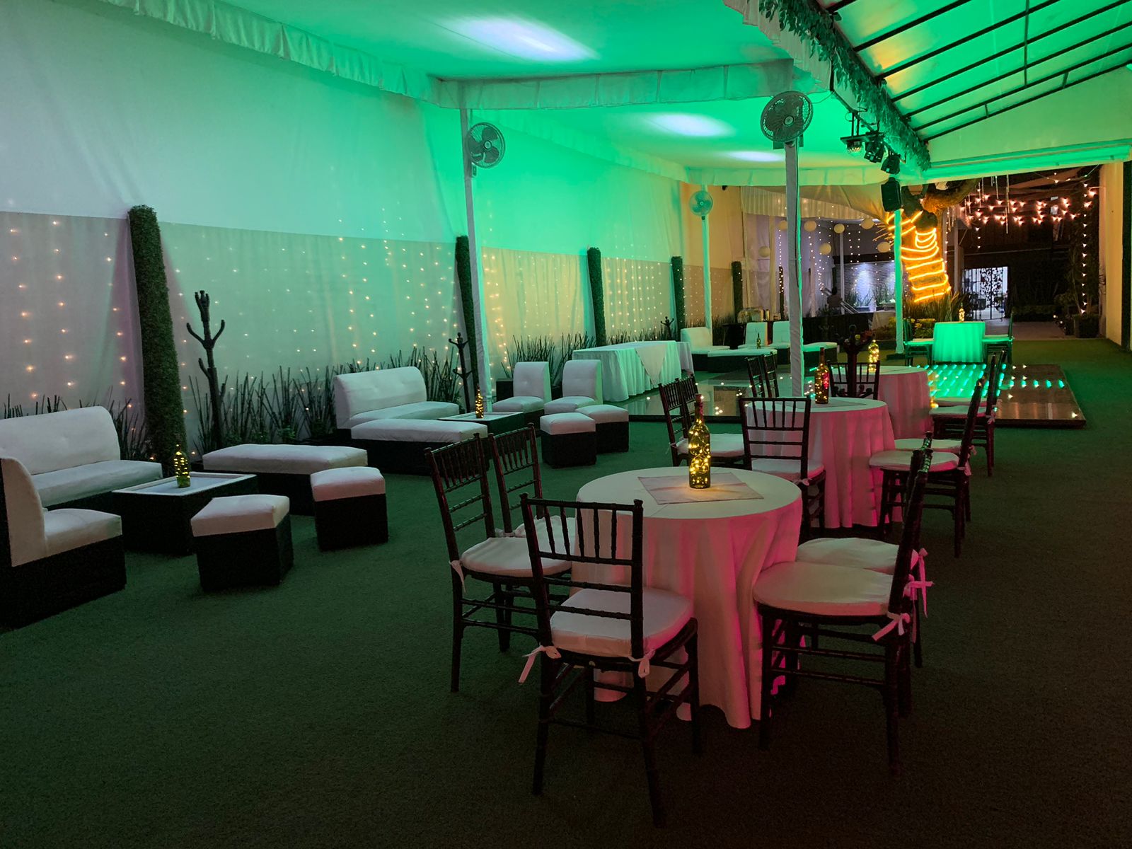 Carpa lounge con iluminación verde, salas blancas y mesas de mantel rosa