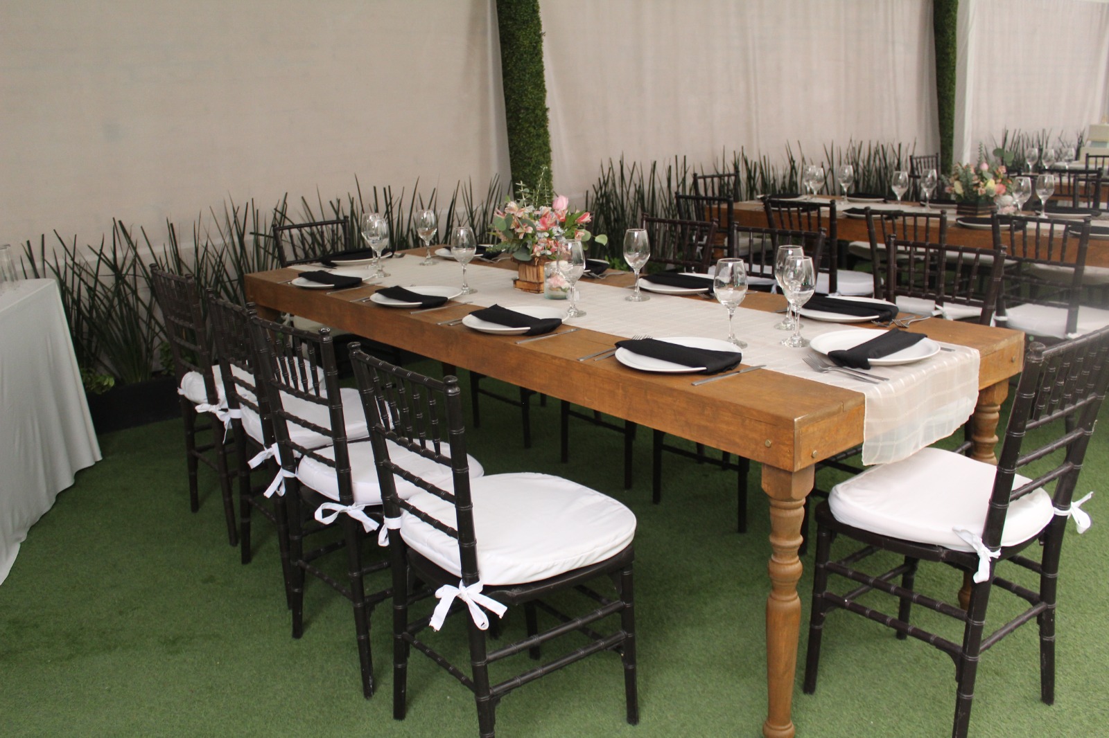 Mesa larga de madera con sillas negras, mantel claro y servilletas negras