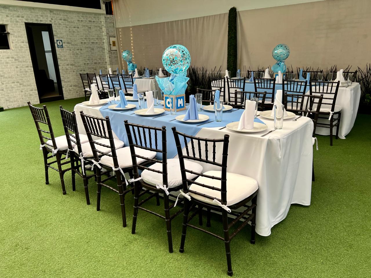 Mesas con mantel blanco, camino azul, globos de confeti y sillas negras