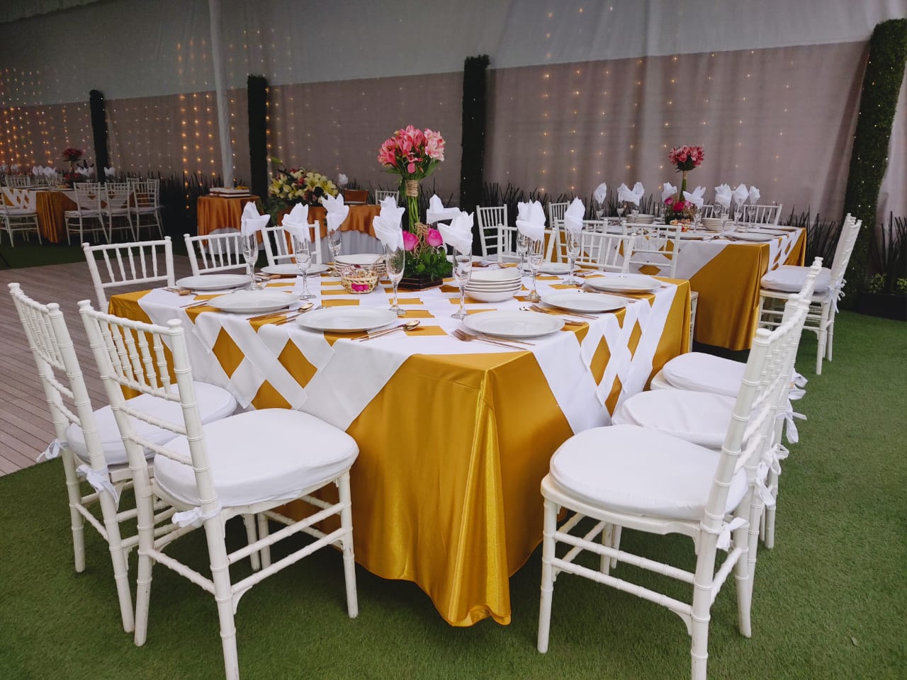 Mesa redonda con mantel blanco y dorado, sillas bambú blancas y flores rosas