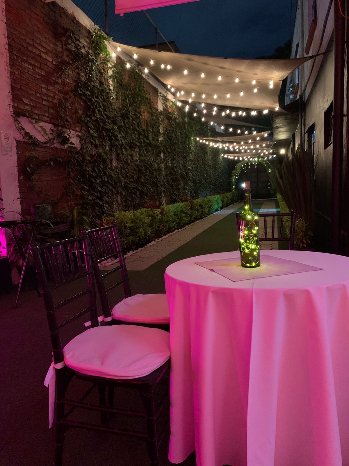 Mesa de lounge al atardecer junto al corredor de muros verdes con luces cálidas