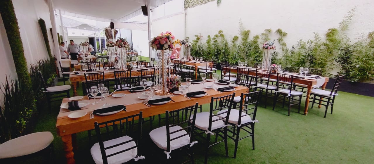 Salón con mesas largas de madera, sillas negras y centros florales en tonos rosas