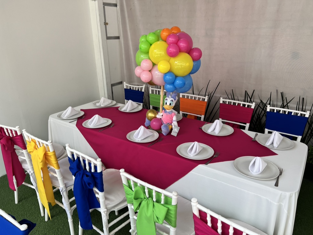 Mesa infantil con mantel fucsia, centro de globos multicolor y personajes para fiestas
