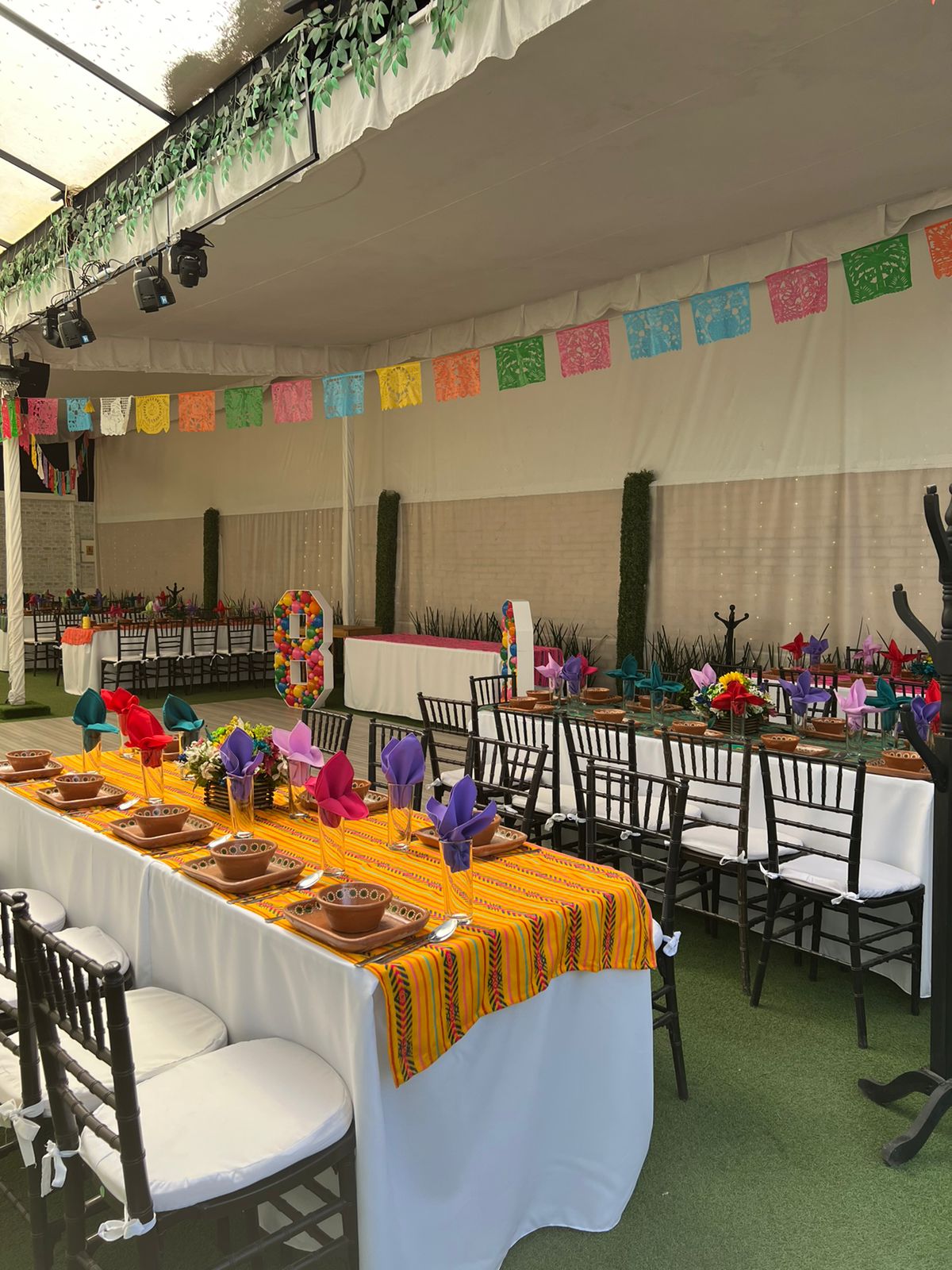 Carpa con mesas de mantel amarillo mexicano, vajilla de barro y globos de colores