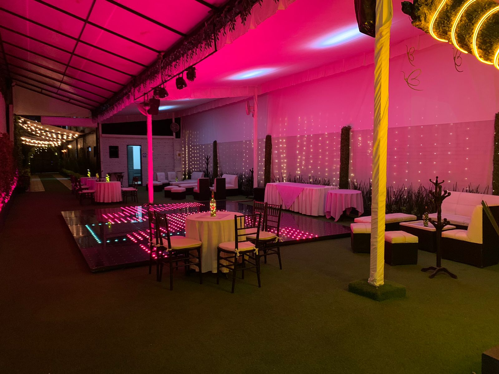 Zona lounge con luces rosas, salas blancas y pista de baile LED bajo la carpa
