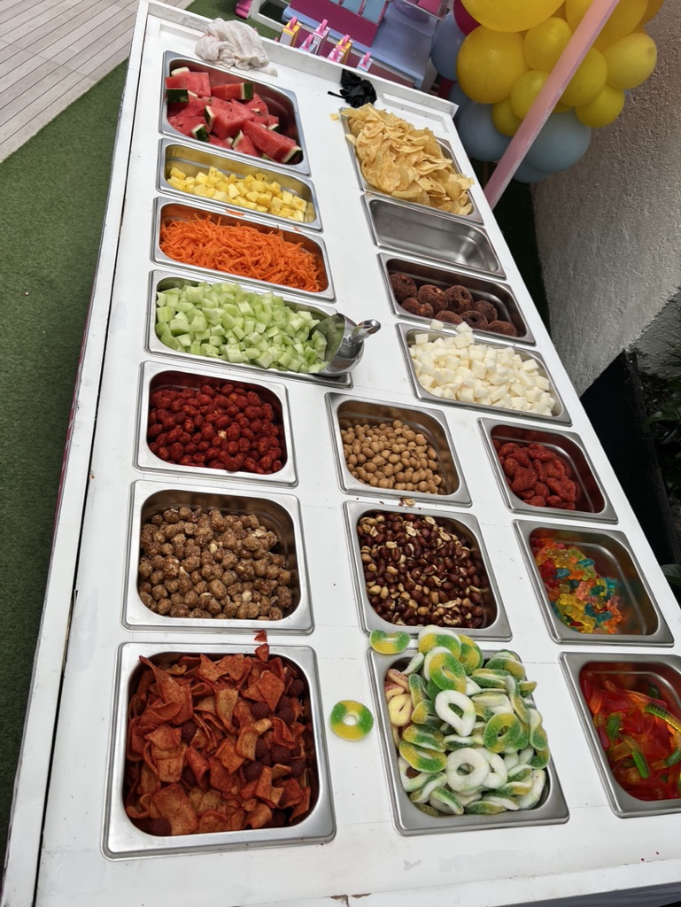 Mesa de snacks y dulces con charolas de frutas, botanas y gelatinas