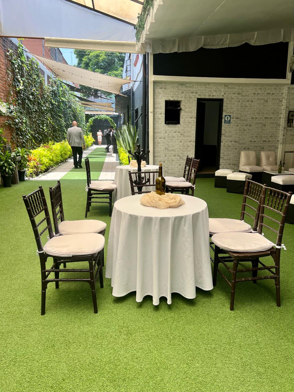 Mesas redondas de lounge con sillas bambú y corredor verde bajo la carpa
