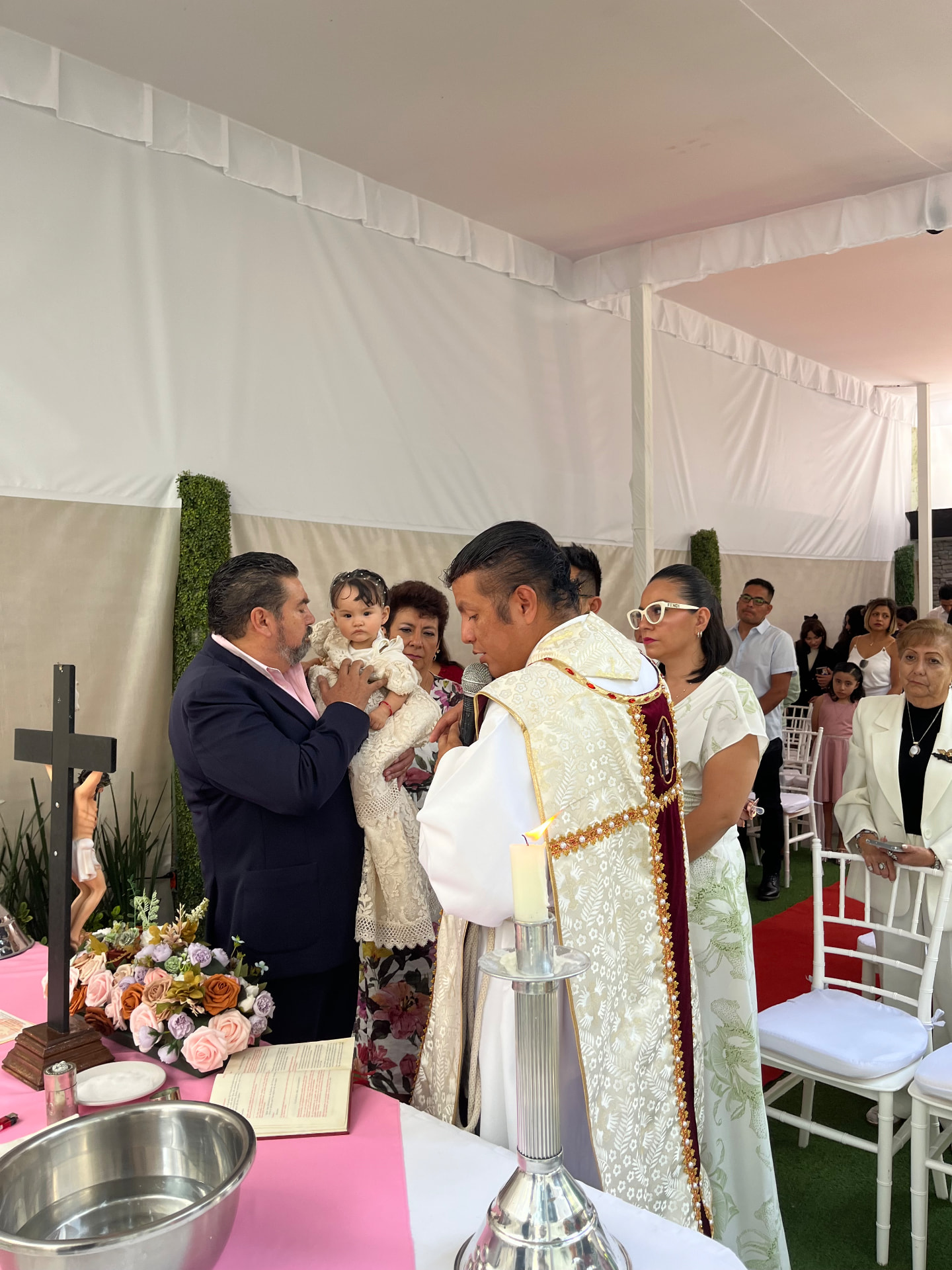Bautizo con sacerdote bendiciendo a la bebé en brazos de su papá junto al altar