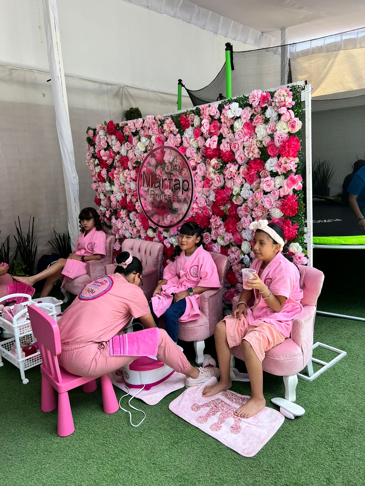 Spa de niñas con muro de flores, sillones rosas y batas a juego