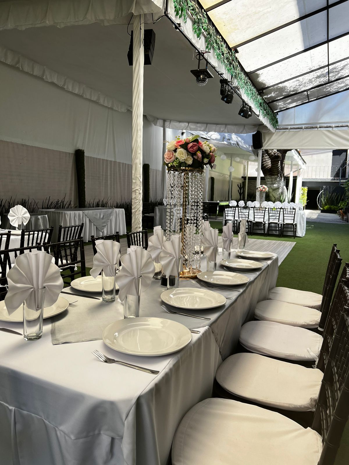 Mesa larga de gala con servilletas blancas en abanico, sillas negras y centro de cristal con flores rosas