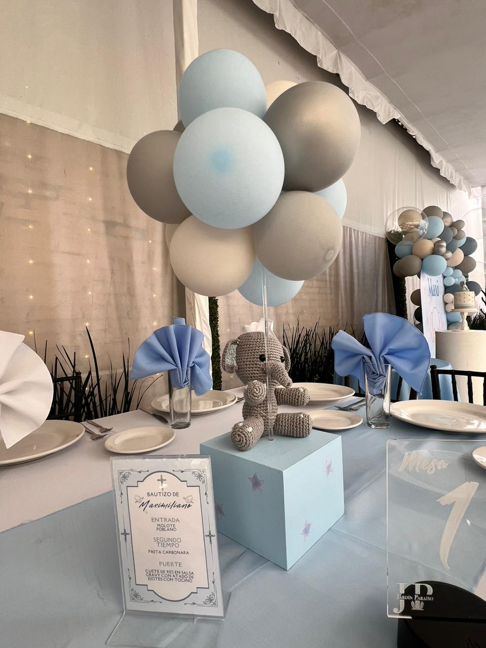 Centro de mesa con globos azules y elefante tejido para bautizo con menú impreso