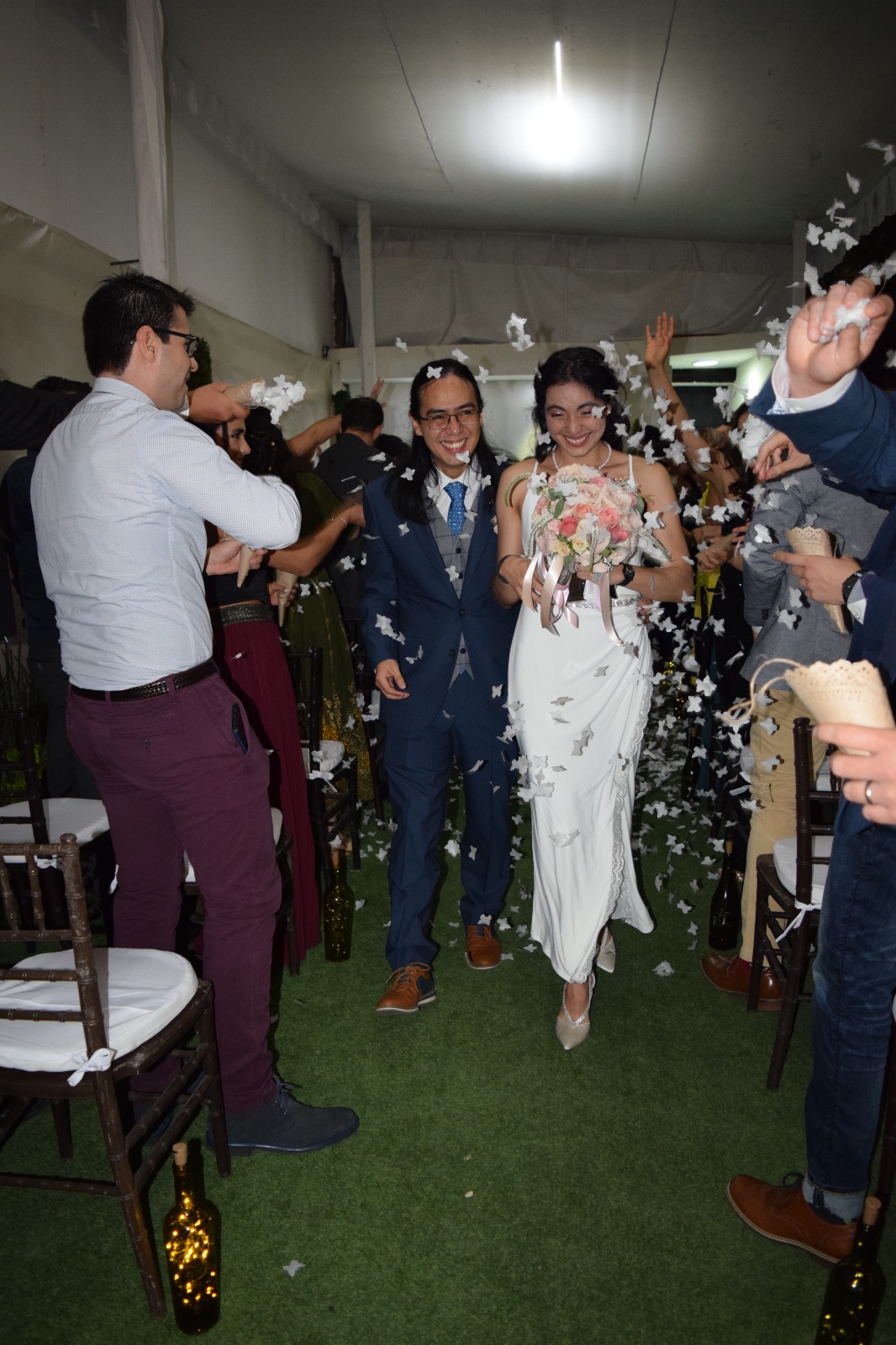 Novios caminando entre mariposas de papel y confeti al finalizar la ceremonia