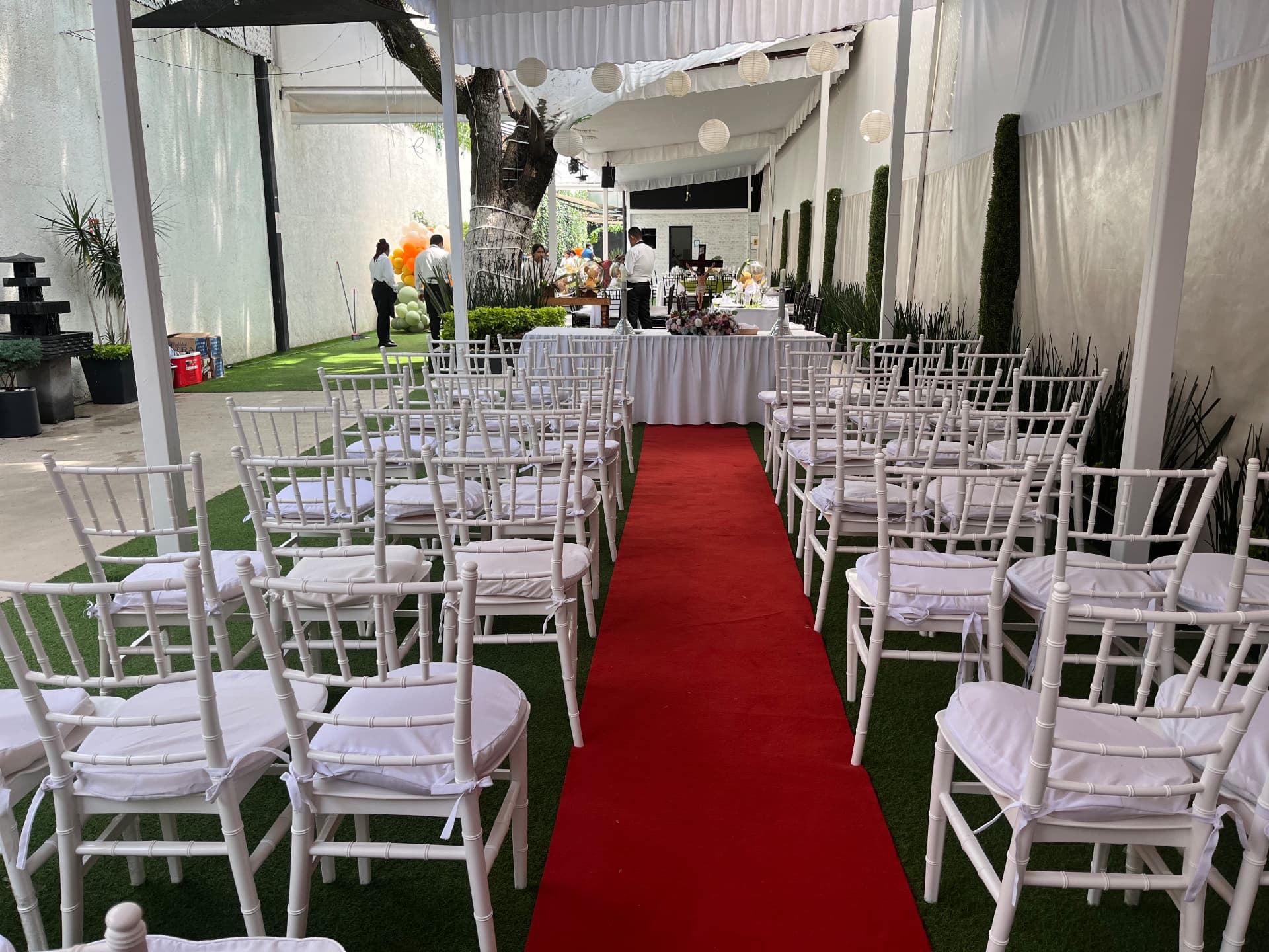 Pasillo de ceremonia con alfombra roja, sillas bambú blancas y farolillos bajo la carpa