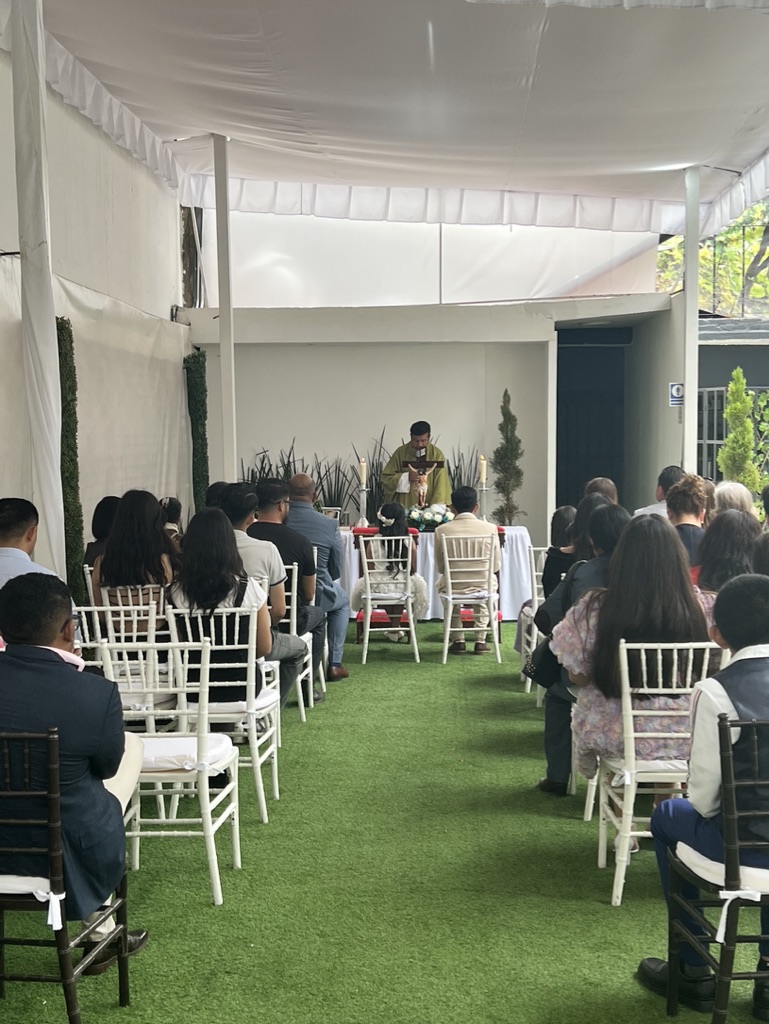 Ceremonia religiosa bajo carpa blanca con sillas bambú frente al altar con sacerdote
