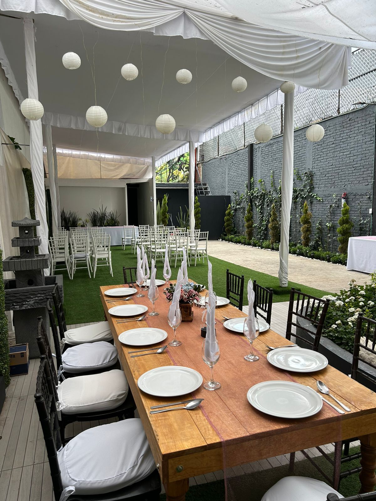 Jardín bajo carpa blanca con farolillos, mesas de madera y flores