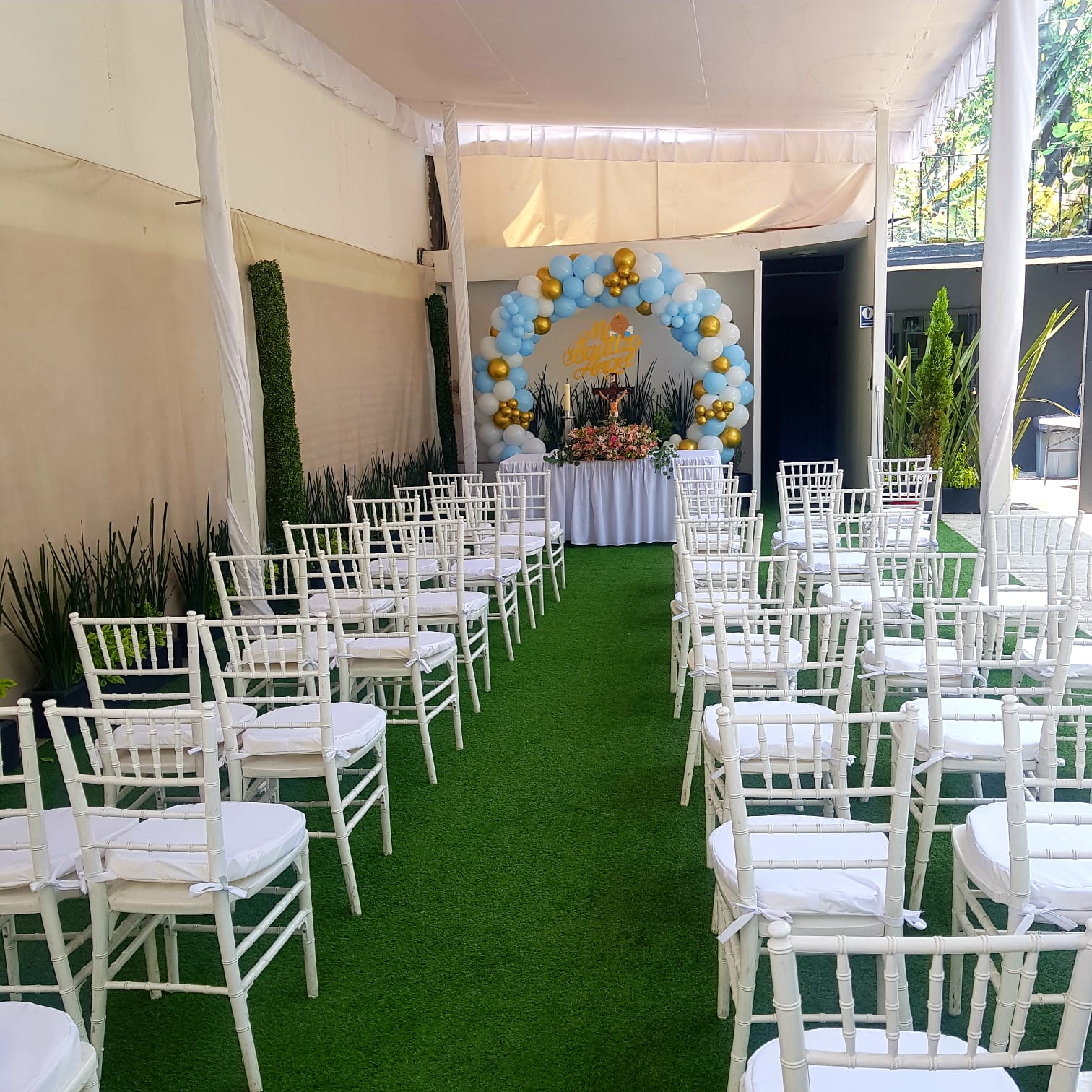 Ceremonia de bautizo con arco de globos azul, blanco y dorado en el jardín
