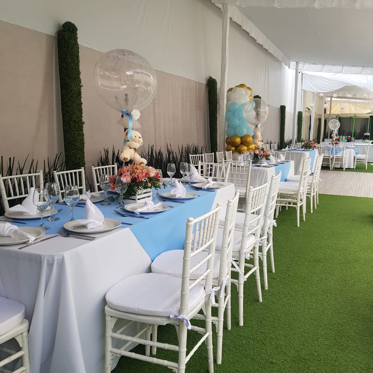 Mesas de bautizo con caminos azules, globos blanco y dorado y centros de osito