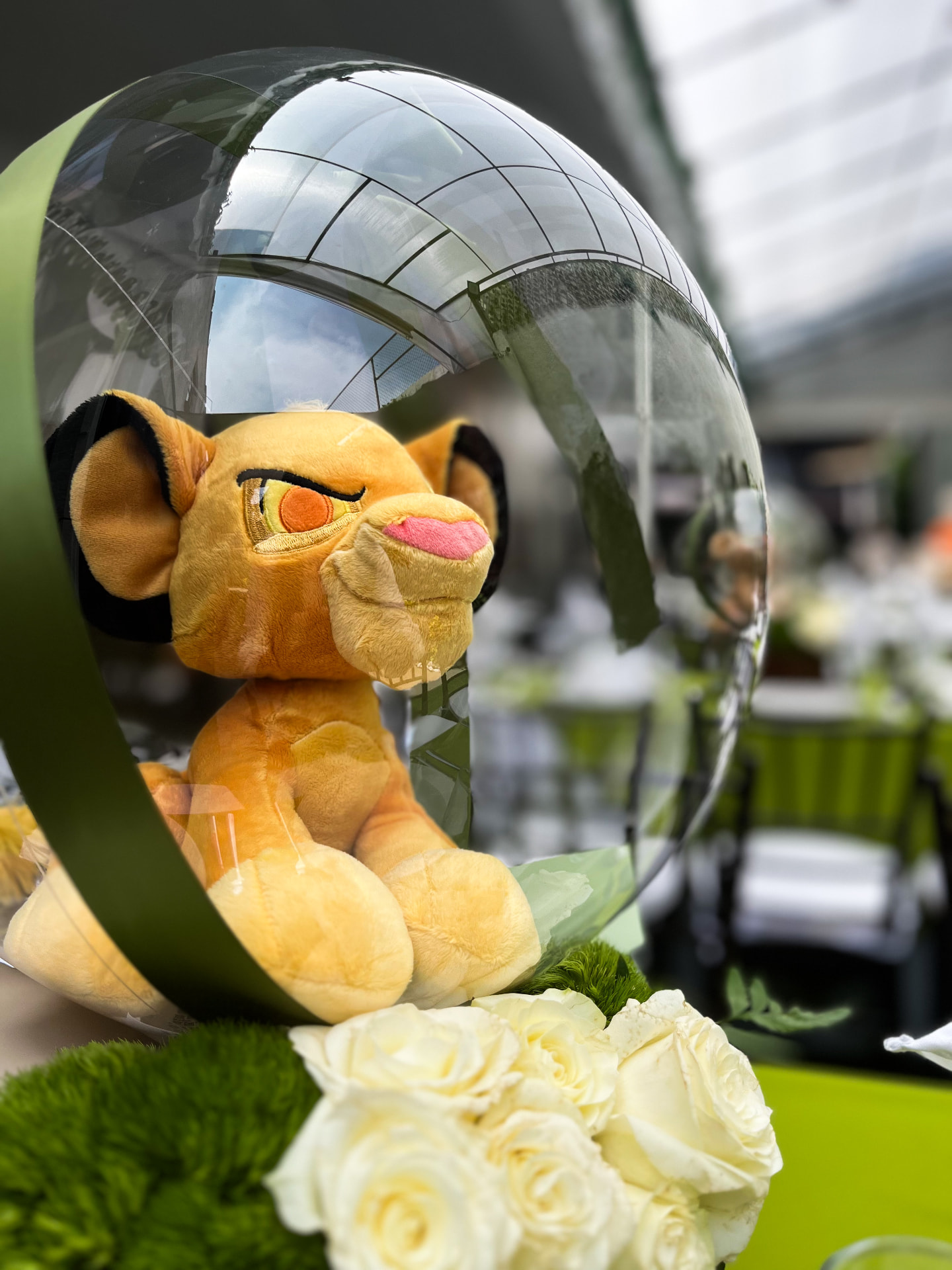 Detalle de centro de mesa con peluche en burbuja transparente y rosas blancas