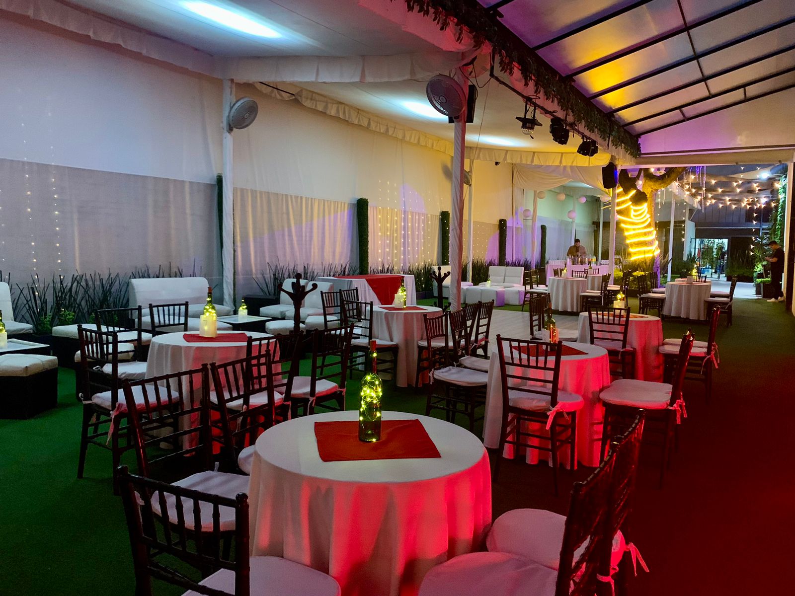 Carpa lounge con mesas de mantel blanco, caminos rojos y salas blancas iluminadas