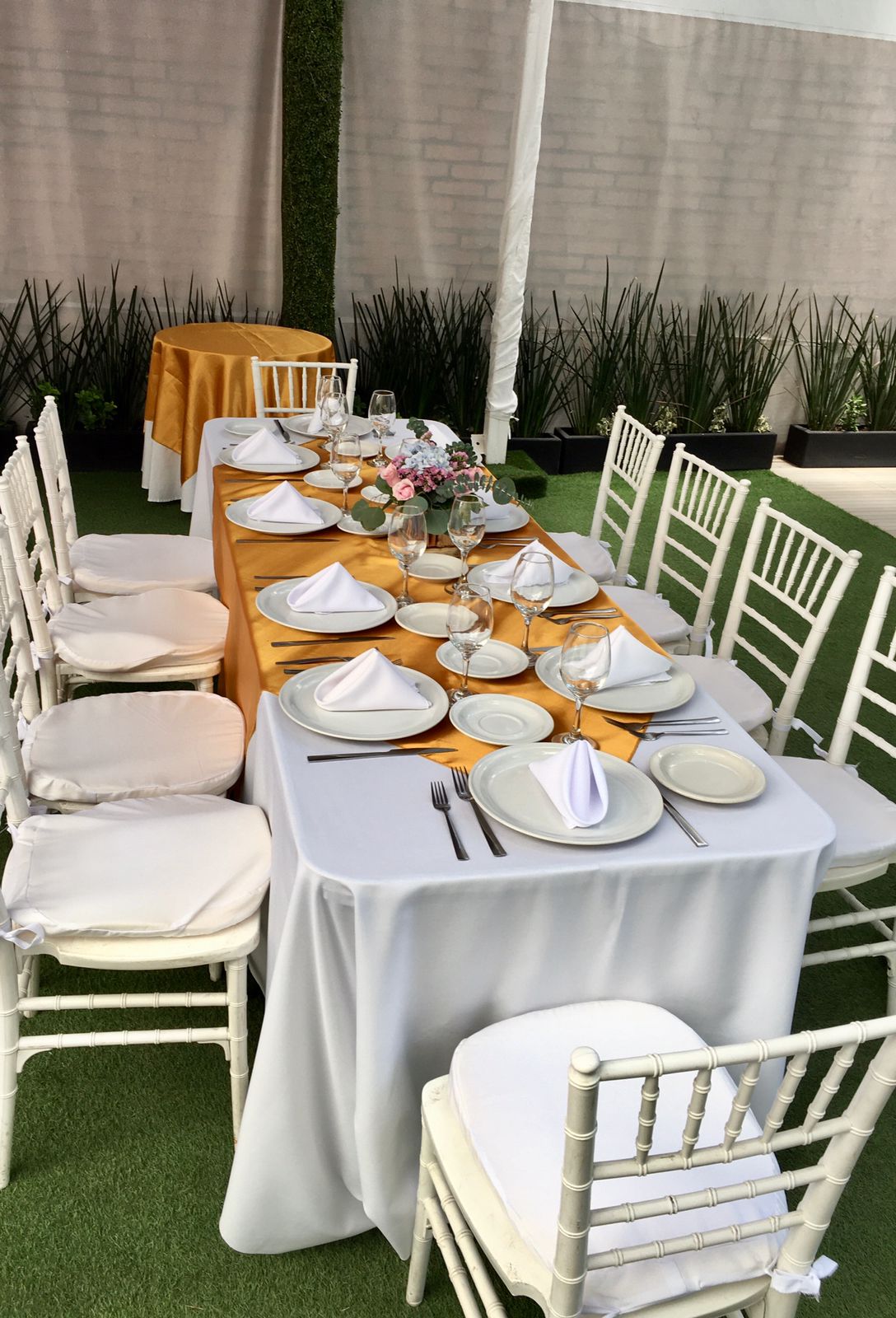 Mesa formal con mantel blanco, camino dorado, sillas bambú blancas y flores rosas