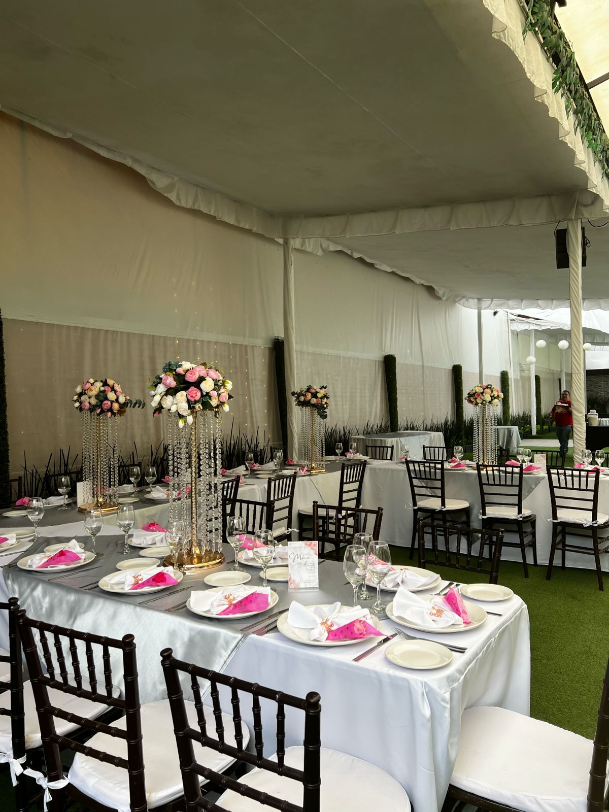 Carpa blanca con mesas de gala, mantel gris, servilletas fucsia y centros de cristal con flores